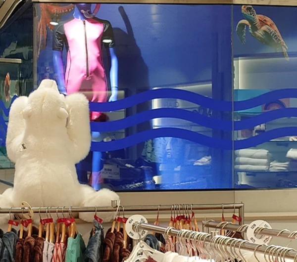 Kinderafdeling van Modehaus Baltz met kleurrijk onderwaterthema, inclusief muurschilderingen van een octopus, schildpad en vissen, naast de roltrap en kledingrekken