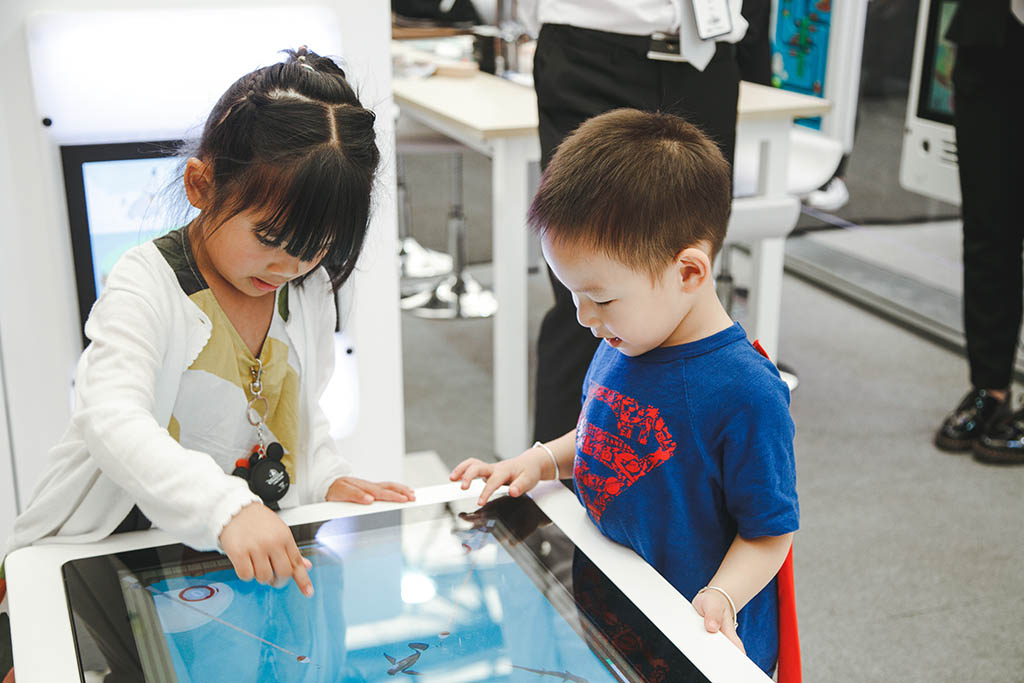 Two children busy playing with the interactive game systems of IKC