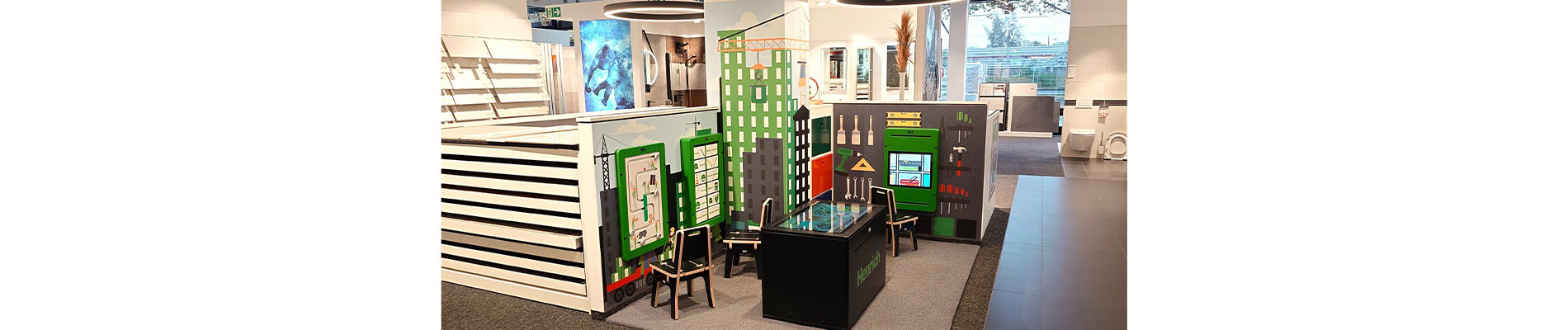 Kinderhoek bij Henrich Baustoffcentrum Siegburg – ontwerp door IKC Speelhoek in de showroom van Henrich Baustoffcentrum in Siegburg, met bouwthema en interactieve wand- en tafelspellen, ontworpen door IKC.