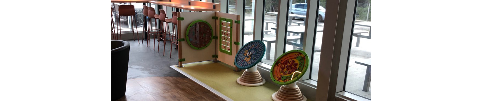 Speelruimte van IKC bij verzorgingsplaats langs de snelweg – een rustpunt voor gezinnen onderweg Kinderhoek met wand- en speelpaneelinstallatie van IKC in een modern wegrestaurant met uitzicht op het buitenzitgedeelte en de parkeerplaats.