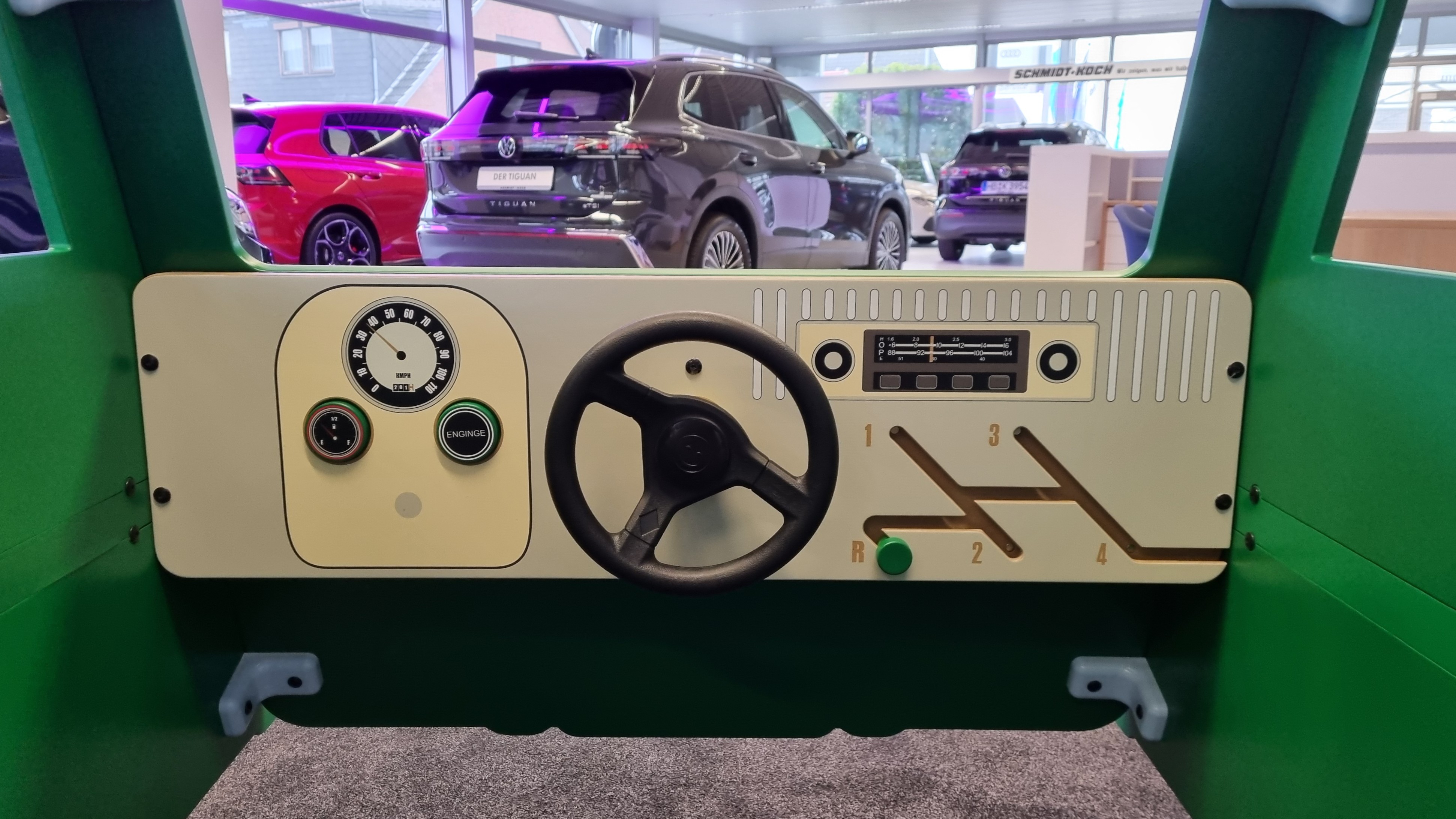 Binnenkant van de op maat gemaakte groene IKC VW-speelbus in de showroom van Autohaus Schmidt + Koch, met een stuur, snelheidsmeter en versnellingspook, ontworpen voor spelend leren en klantbeleving.