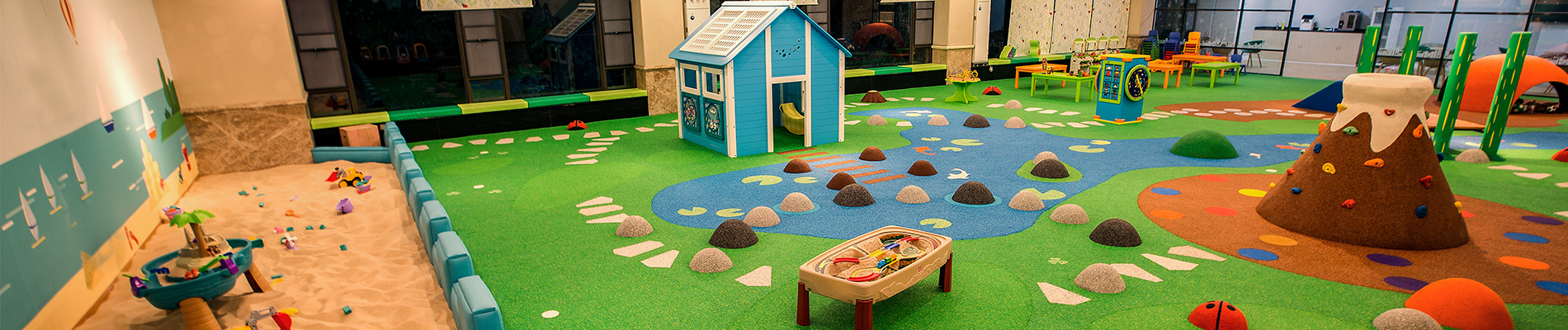Speelruimte in een kinderdagverblijf met een zandbak, klimmuur in vulkaanthema, speelhuis en interactieve speelelementen, ontworpen door IKC.