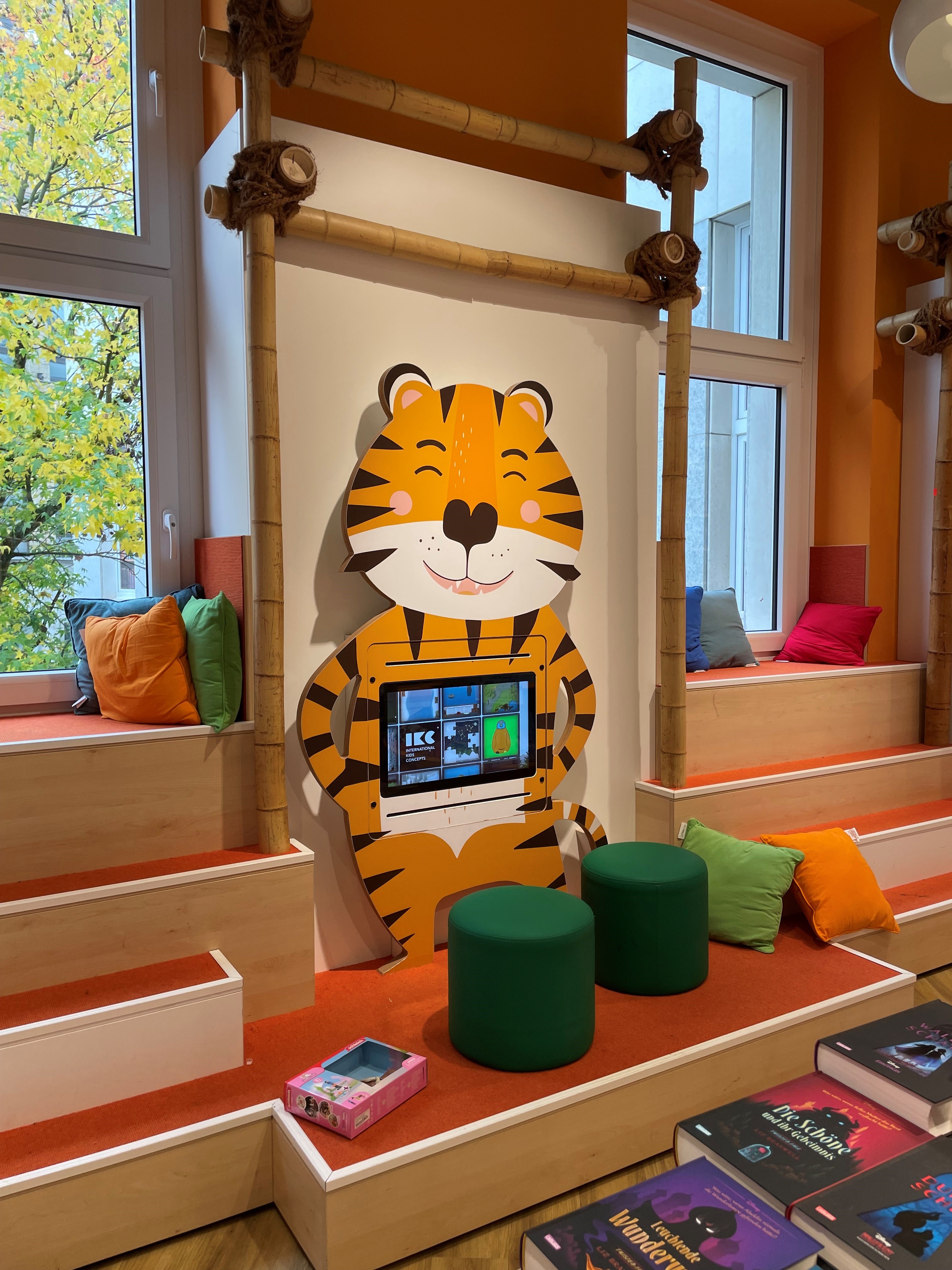 Coin enfants avec écran interactif tigre – Librairie Thalia Krefeld Espace enfants coloré avec un écran interactif intégré dans une borne en forme de tigre, installé dans la librairie Thalia à Krefeld.